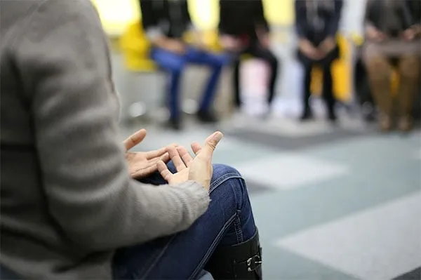 Una persona parla gesticolando davanti a un gruppo seduto in cerchio