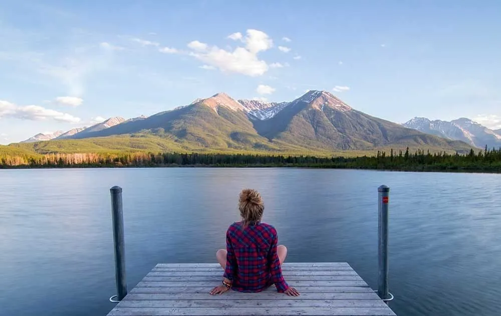 Una donna seduta su un pontile medita davanti a un lago di montagna